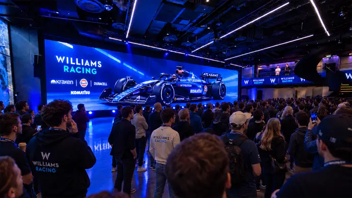A crowd facing a wide LED wall showing the Atlassian Williams Racing car and its sponsors, with Williams Racing screens along the balcony above