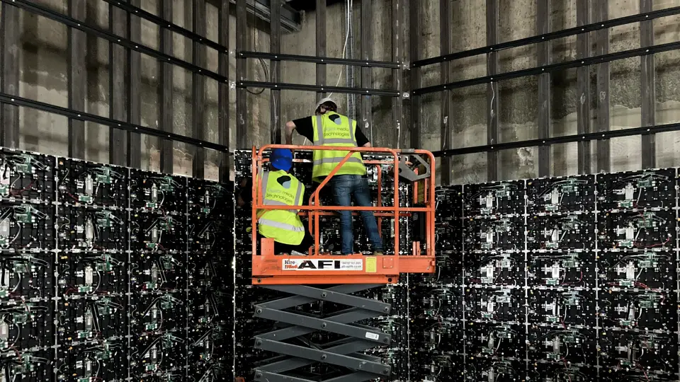 Two DMT technicians on a scissor lift fitting LED panels to a steel frame on a bare wall